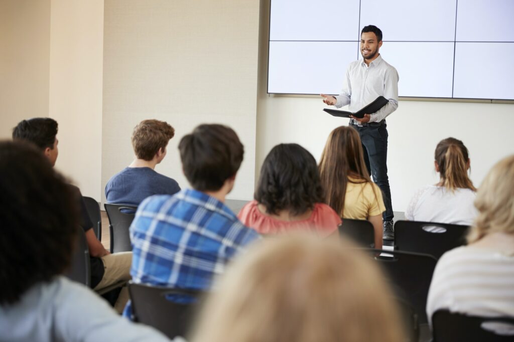 Teacher Giving Presentation To High School Class In Front Of Screen