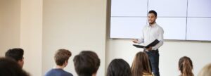 Teacher Giving Presentation To High School Class In Front Of Screen