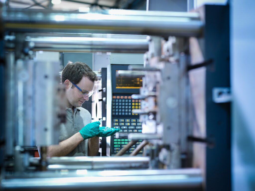 Worker inspecting parts from plastic injection moulding machine in plastics factory